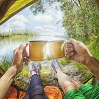 Young couple sitting in the tent and drinking tea while looking on the Desna river , Ukraine