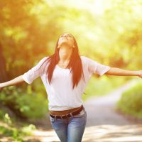 Happy young beautiful woman in park having fun with outstreched arms. About 20 years old, Caucasian brunette.