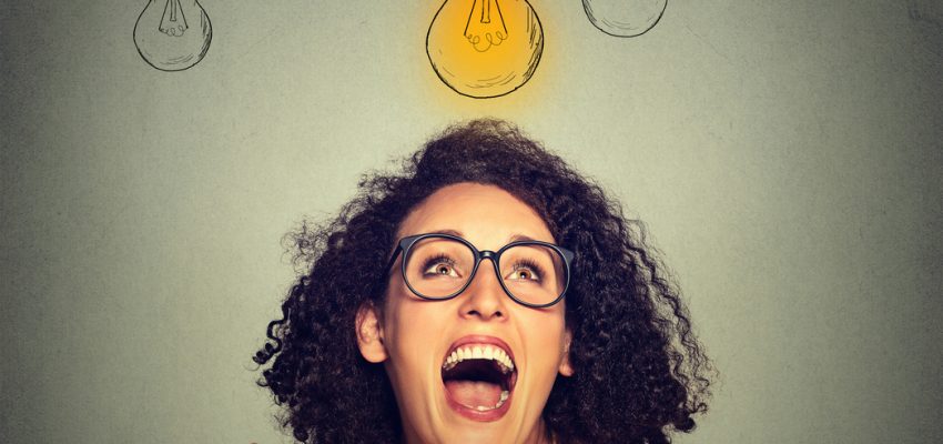 Portrait super happy excited woman in glasses looking up at bright light idea bulb above head isolated on gray wall background
