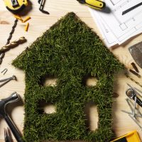 Grass house cut out with construction tools on a wooden background.