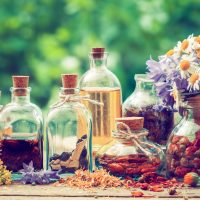 Bottles of tincture or potion and dry healthy herbs, bunch of healing herbs in wooden box on table outdoors. Herbal medicine. Retro styled.